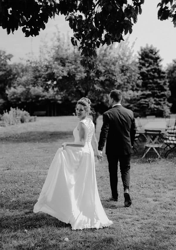 Braut mit einem Brautkleid mit Spitzenrücken läuft in einen Garten