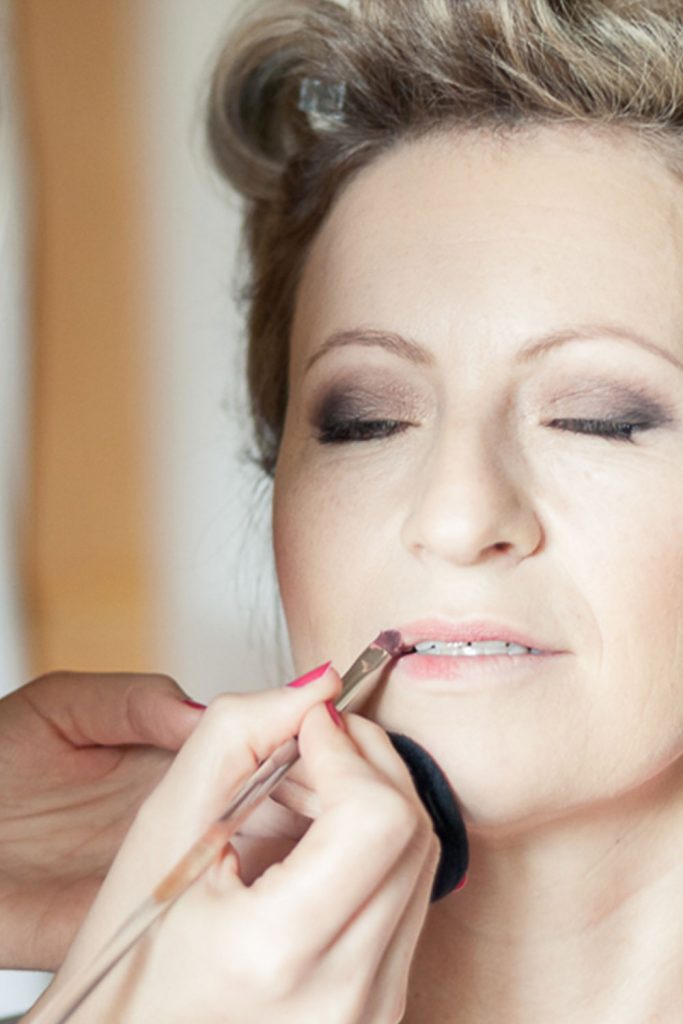 Visagistin probiert Lippenstift an Braut