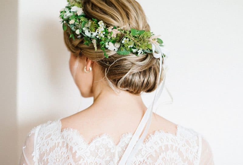 Brautfrisur mit tiefem Dutt und grünem Blumenkranz von hinten