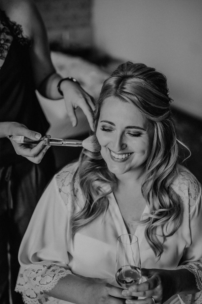 Entspannte Braut genießt die zarten Berührungen ihrer Visagistin im Gesicht