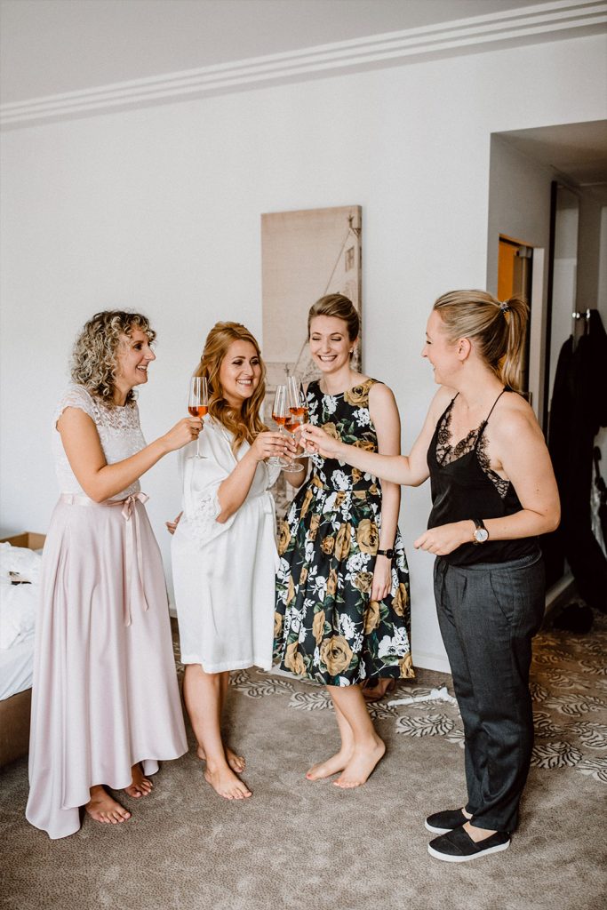Brautstylistin stößt mit Braut, Trauzeugin und Freundin auf die Hochzeit an