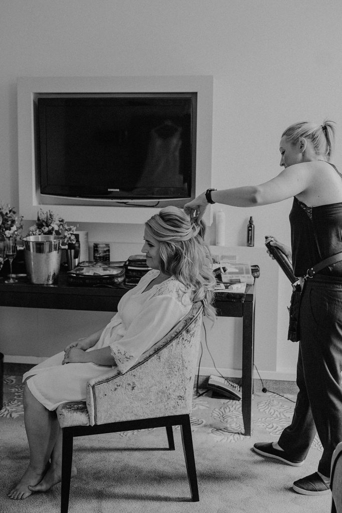 Brautstylistin macht Haarstyling von Braut im Hotelzimmer