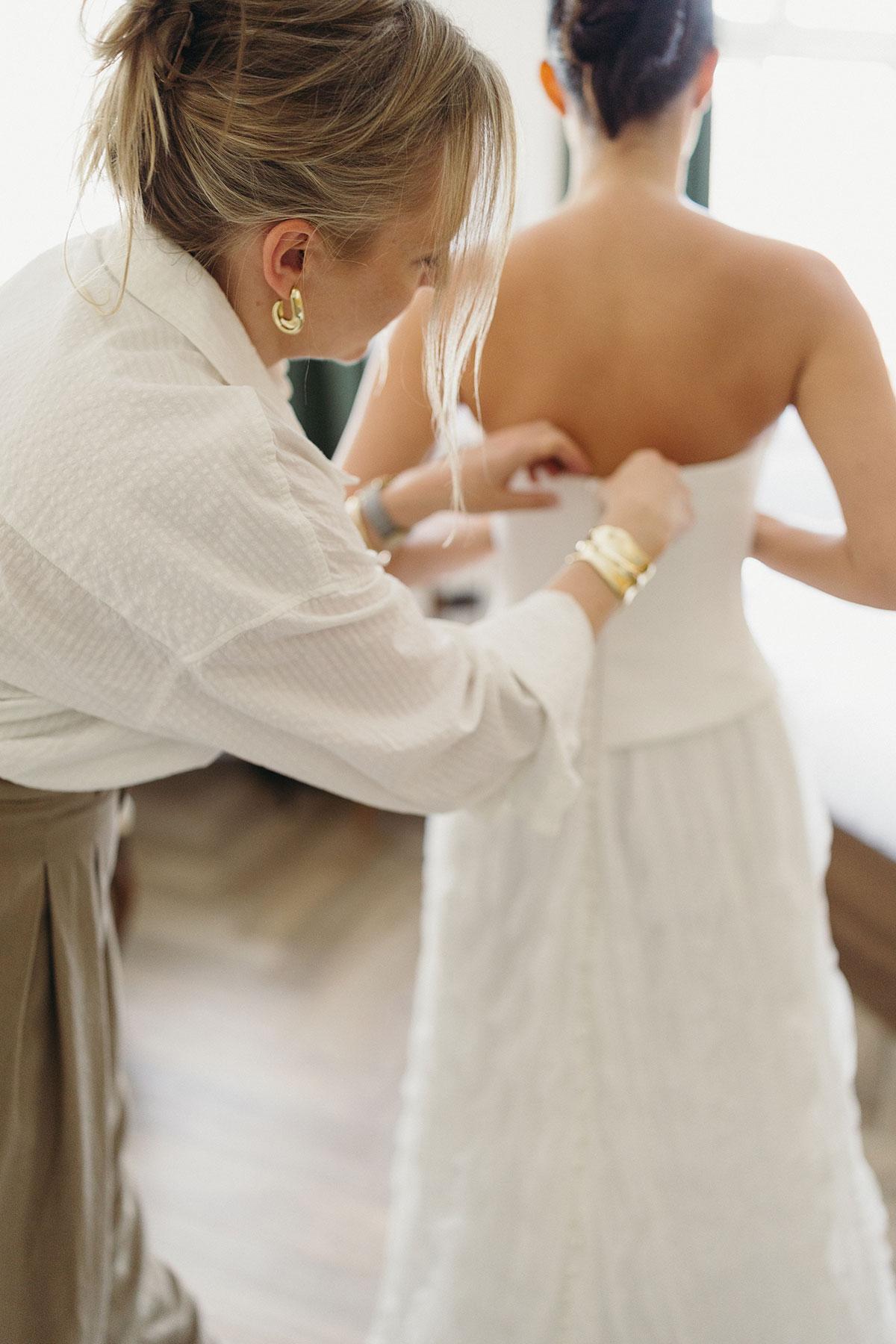 Stylistin unterstützt die Braut bei den letzten Details ihres Brautkleides während des Getting Ready.